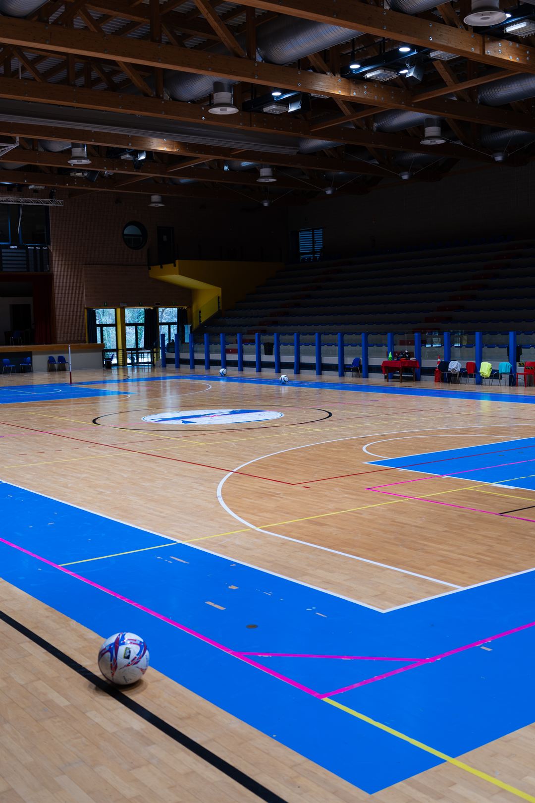 Spielfeld der Sporthalle mit Holzboden und blauen Markierungen, vorne ein Ball